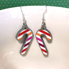 Load image into Gallery viewer, Silver glitter candy cane dangle earrings hung over the edge of a mug. The stripes on the candy cane are those of the Lesbian flag; Orange, Pink, and White.