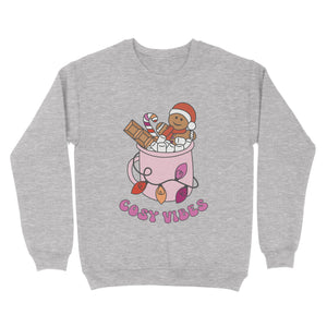 Heather Grey sweatshirt featuring retro text reading 'cosy vibes'. The image shows a mug of hot chocolate with marshmallows and a gingerbread man wearing a Santa hat. A candy cane in the mug and lights around the mug are the colours of the lesbian pride flag.