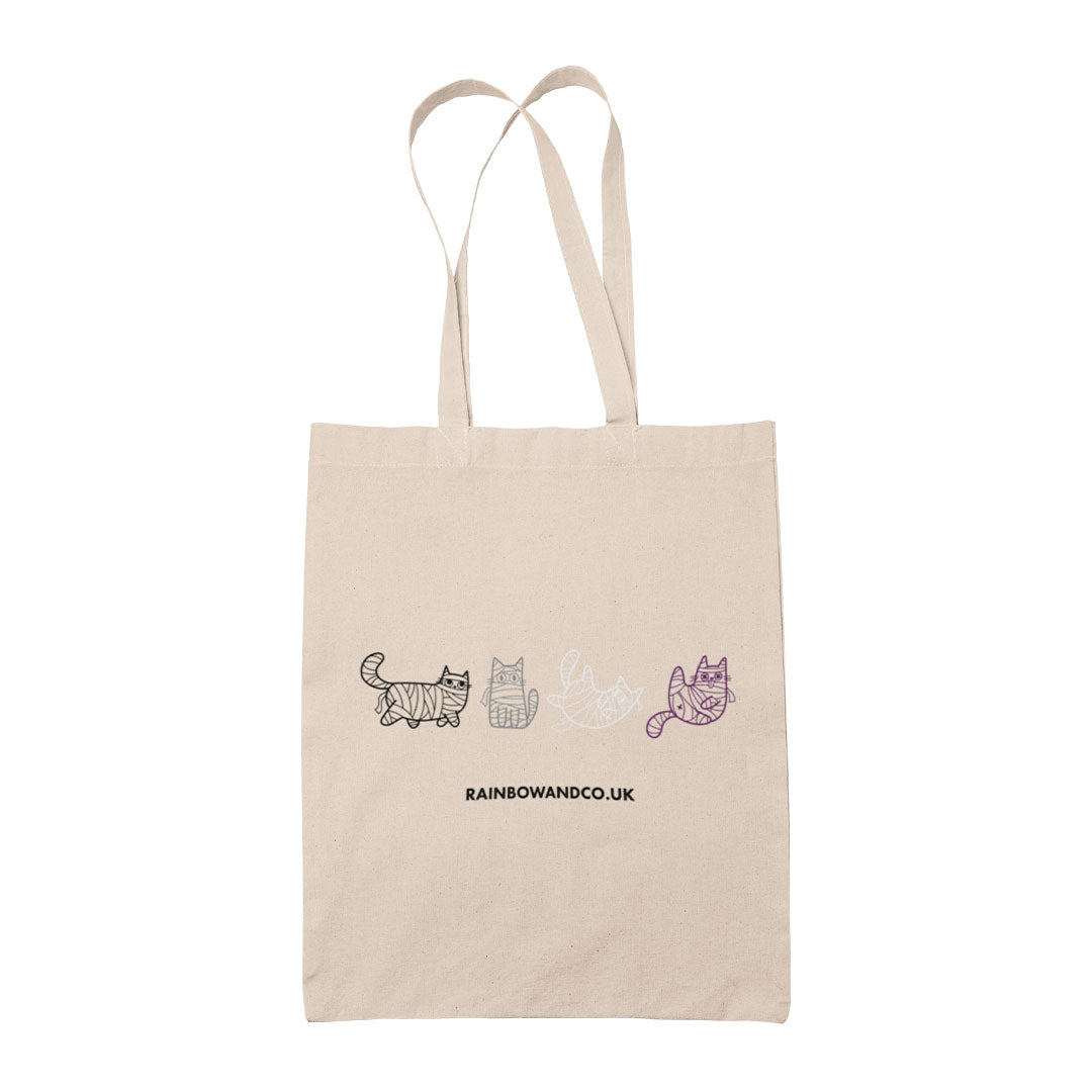 A natural canvas tote bag featuring a line drawing of four mummy cats in varying shades of grey and purple, symbolising the Asexual pride flag. The design includes cute mummy-wrapped cats in different poses.