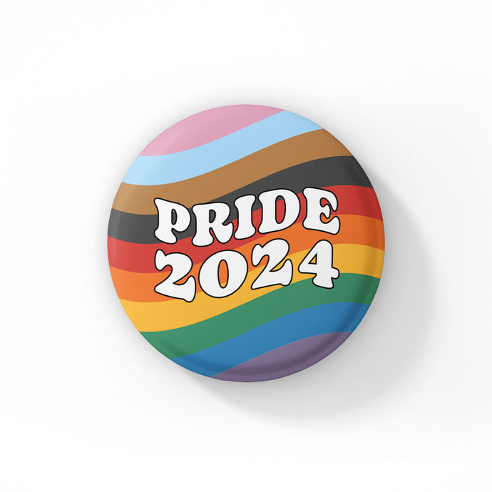 38mm Badge on a white background. The badge features the colours of the progress pride flag in waving lines across the background with retro style white typography in the foreground reading Pride 2024