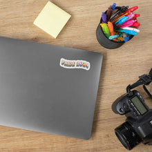 Load image into Gallery viewer, Pride 2024 sticker on a laptop cover with coloured pens and a camera beside it.