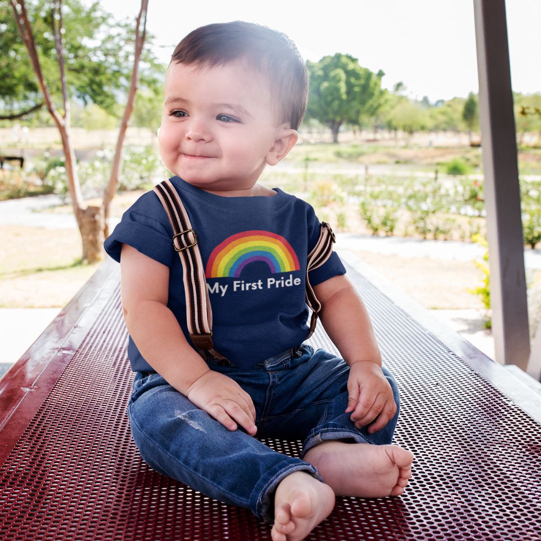 A young child with short dark hair wearing blue jeans with fabric braces and a navy blue My First Pride t shirt from Rainbow & Co