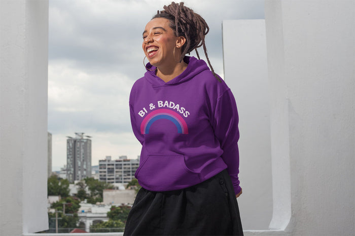 A person with locs tied up in a bun, wearing large hoop earrings and a bright purple hoodie that reads 