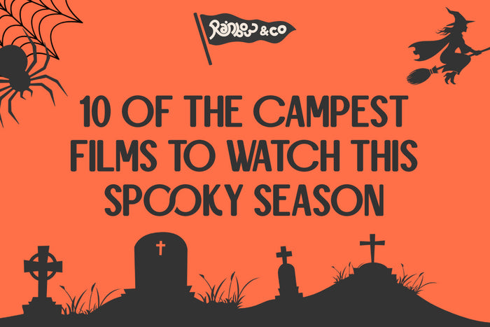 Bright orange Halloween-themed graphic with black silhouettes of a spider, cobweb, flying witch, and graveyard. The Rainbow & Co flag logo appears at the top. Bold black text in the centre reads: “10 of the Campest Films to Watch This Spooky Season.” The 