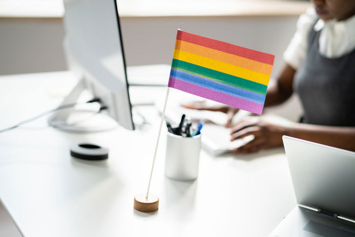 Office desk with a hand held rainbow pride flag sat on it.