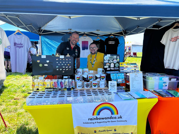 The Rainbow & Co stall at York Pride 2023. Adam stands behind the stall with friend David Krushell from Evolve Your Digital. 