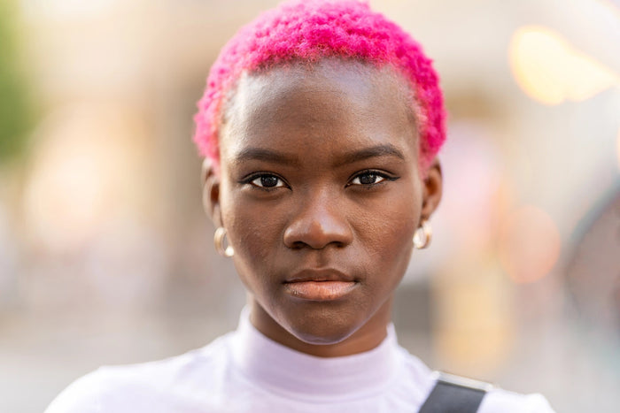 Close-up portrait of a woman with short bright pink hair looking directly at the camera with a calm, confident expression, symbolising self-acceptance and queer identity.