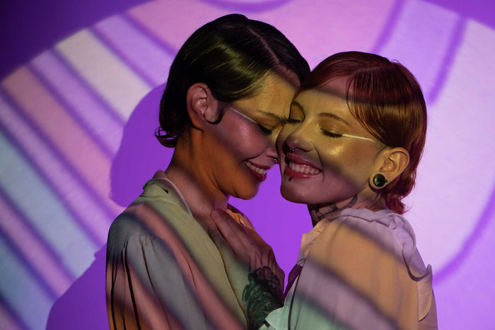 Queer couple embracing under colourful light projections