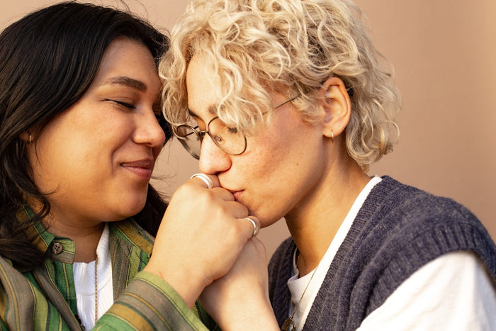 Close up of a queer couple, person on the right is kissing the hand of the person on the left.