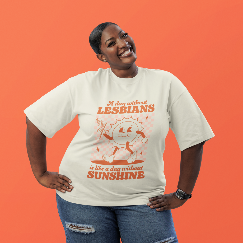 Model wearing a vintage white T-shirt with a retro cartoon sun and the slogan “A day without lesbians is like a day without sunshine” against an orange background.