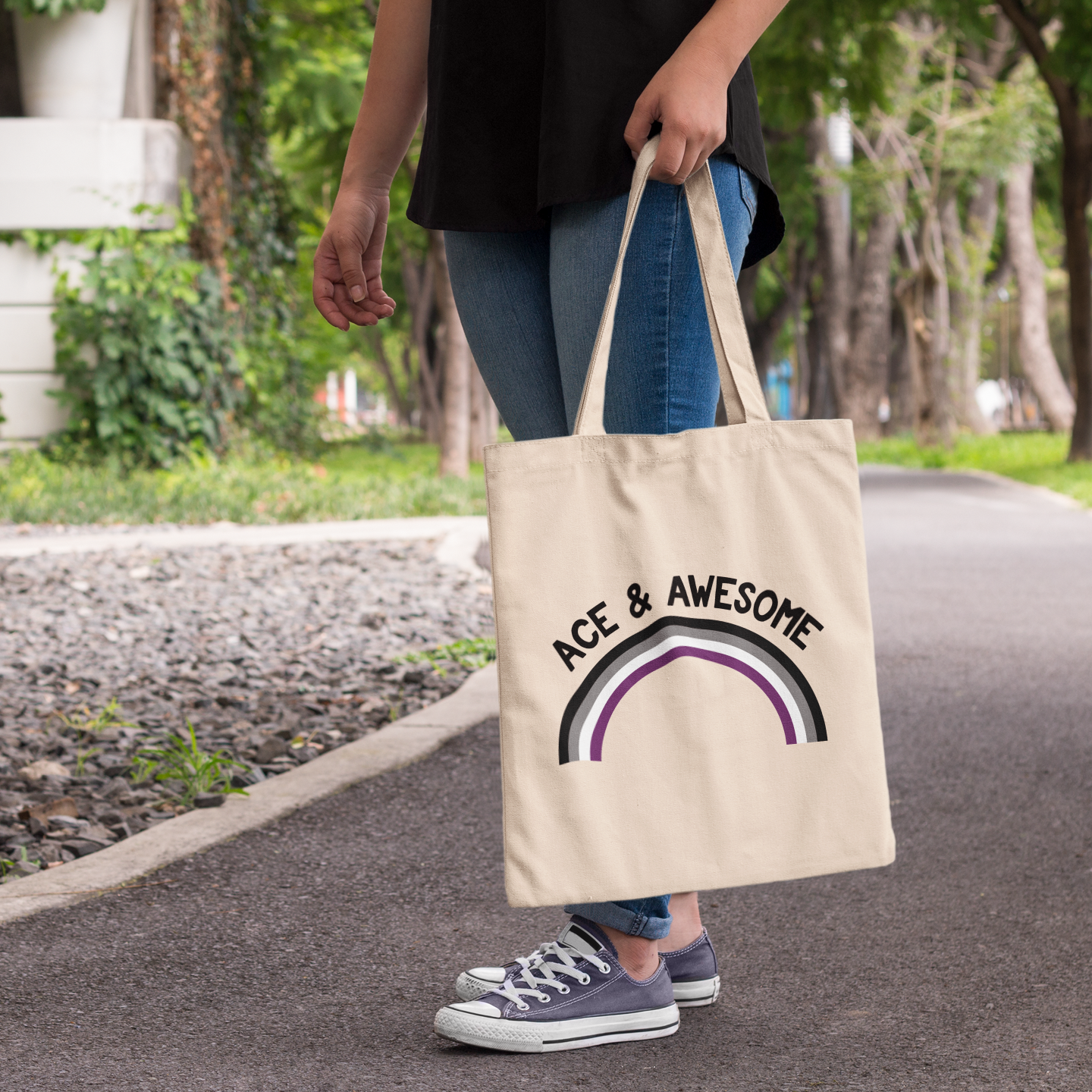 Natural cotton tote bag with “Ace & Awesome” text and an asexual pride rainbow, shown being carried outdoors.