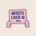 Artists Over AI vinyl sticker featuring illustrated hands holding a pink protest sign with the words "Artists Over AI".