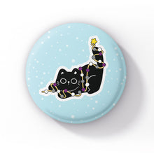 Load image into Gallery viewer, A black cat tangled in string lights in the colours of the asexual flag (black, grey, white, and purple), playfully lying down against a light blue background with snowflakes.