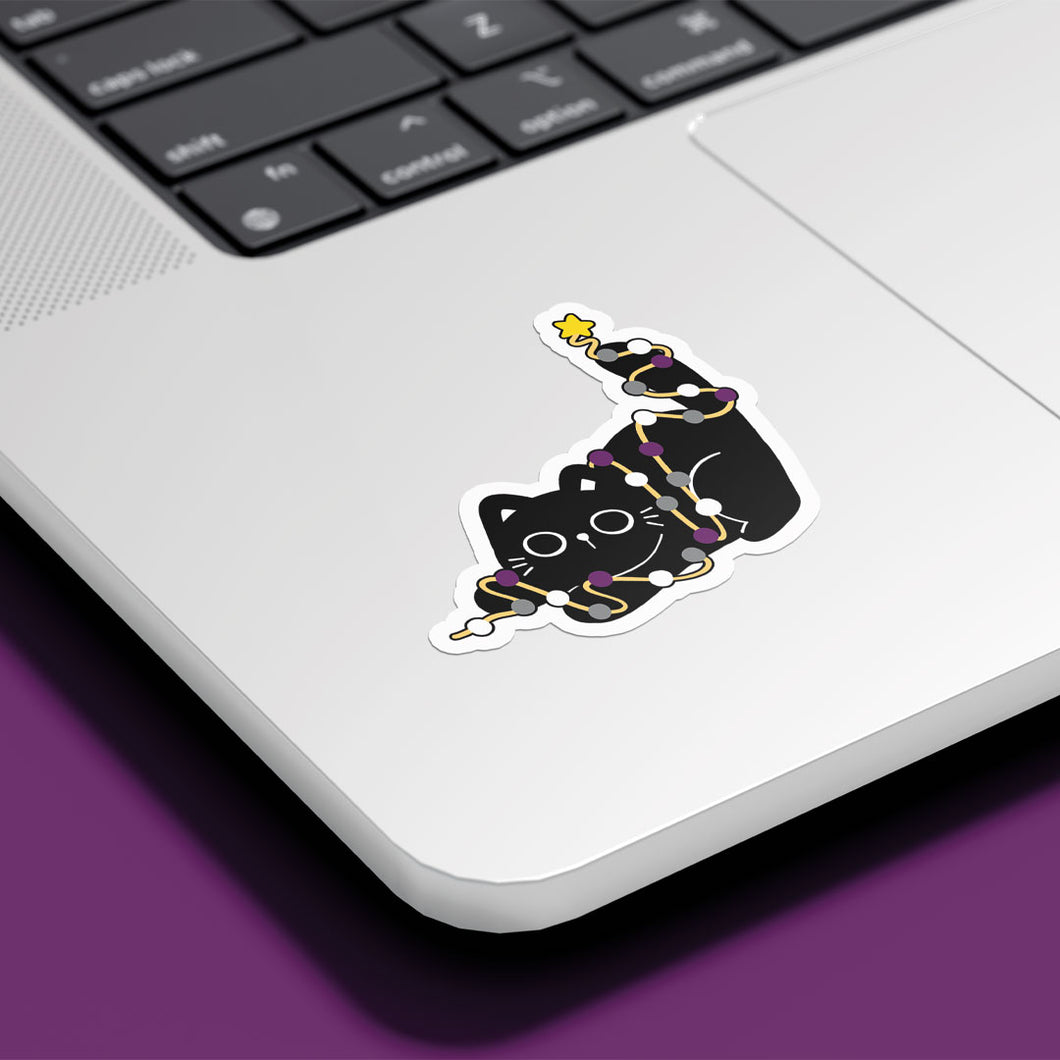 A cute black cat, wrapped in Asexual pride-coloured string lights (purple, black, white, grey), reaches upwards with a yellow star on its paw. The sticker is placed on the silver surface of a laptop.