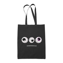 Load image into Gallery viewer, A black tote bag with three cartoonish eyeballs in a row. The eyeballs have varying colours: one with a black iris, one with a grey iris, and one with a purple iris. Below the eyeballs is the text &quot;RAINBOWANDCO.UK&quot;.