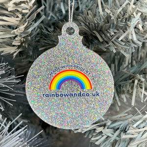 Close up of a white Christmas tree displaying the back of a silver glitter bauble featuring the text 'Made With Pride By' and the Rainbow & Co logo with website address, rainbowandco.uk