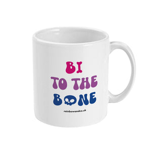 A white ceramic coffee mug with the handle on the right. The mug shows the slogan 'Bi To The Bone' in the colours of the bisexual flag with a bone and a skull icon.