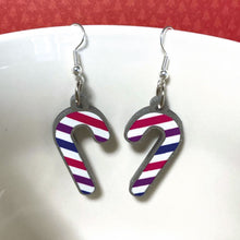 Load image into Gallery viewer, Silver glitter candy cane dangle earrings hung over the edge of a mug. The stripes on the candy cane are those of the Bisexual flag; pink, purple, and blue.