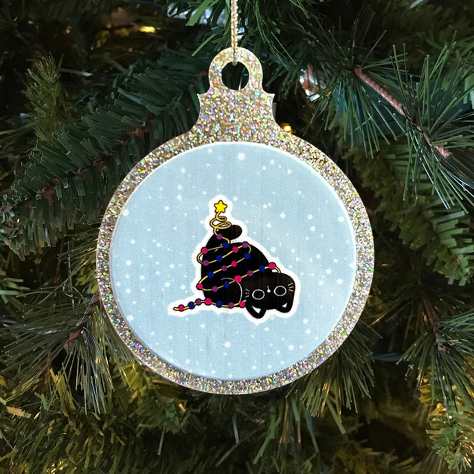 A glittery Christmas bauble featuring a black cat wrapped in colourful fairy lights in the colours of the bisexual pride flag. The cat sits playfully with a star on its tail against a snowy background, hanging on a festive tree.