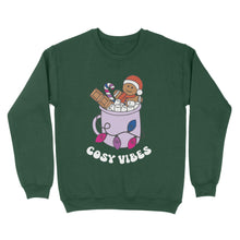 Load image into Gallery viewer, Bottle Green sweatshirt featuring retro text reading &#39;cosy vibes&#39;. The image shows a mug of hot chocolate with marshmallows and a gingerbread man wearing a Santa hat. A candy cane in the mug and lights around the mug are the colours of the bisexual pride flag.