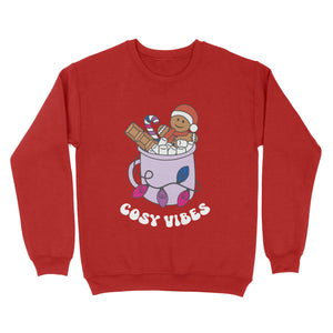 Fire Red sweatshirt featuring retro text reading 'cosy vibes'. The image shows a mug of hot chocolate with marshmallows and a gingerbread man wearing a Santa hat. A candy cane in the mug and lights around the mug are the colours of the bisexual pride flag.