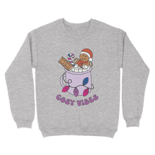 Load image into Gallery viewer, Heather Grey sweatshirt featuring retro text reading &#39;cosy vibes&#39;. The image shows a mug of hot chocolate with marshmallows and a gingerbread man wearing a Santa hat. A candy cane in the mug and lights around the mug are the colours of the bisexual pride flag.