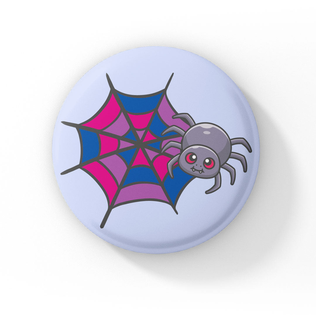A circular badge with a cute grey spider with pink eyes on a web coloured in pink, purple, and blue, representing the bisexual pride flag. The badge has a light blue background.