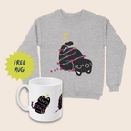 Grey Christmas jumper featuring an upside-down black cat wrapped in pink, purple and blue fairy lights, alongside a white mug with matching bisexual pride colours. Both sit on a cream background, with a lime-green starburst reading “FREE MUG!”