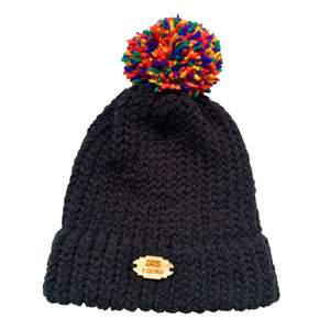 Black knitted bobble hat with pom pom in the colours of the rainbow pride flag laying flat.