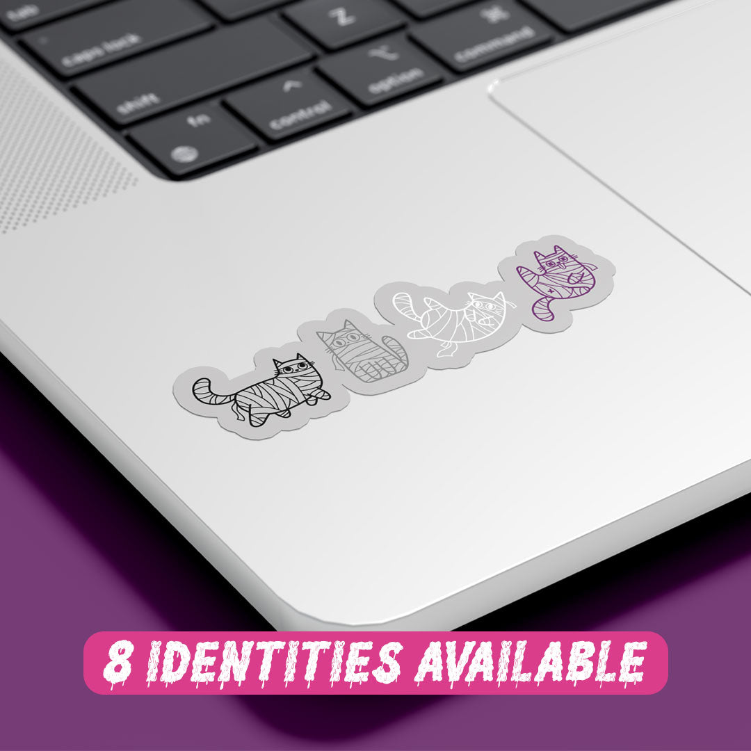 A silver laptop with a sticker featuring four mummy-wrapped cats in monochrome colours. The cats are positioned in a row on the bottom right corner of the laptop's surface. Below the sticker, there is a pink banner with white text that reads "8 IDENTITIES AVAILABLE."