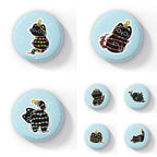 Image featuring a collection of round badges, each displaying a playful black cat tangled in colourful festive string lights, set against a light blue background with white snowflake-like spots. Each badge showcases the cat in different playful poses, with various pride flag colours represented in the lights, including rainbow, transgender, non-binary, and more.