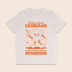 A vintage white short-sleeve crewneck t-shirt with a retro-style orange graphic on the front. The graphic features a cartoon sun character holding a flag and the text 'A day without LESBIANS is like a day without SUNSHINE'.