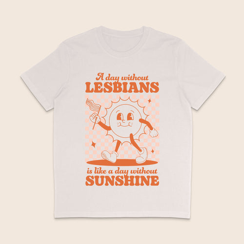 A vintage white short-sleeve crewneck t-shirt with a retro-style orange graphic on the front. The graphic features a cartoon sun character holding a flag and the text 'A day without LESBIANS is like a day without SUNSHINE'.