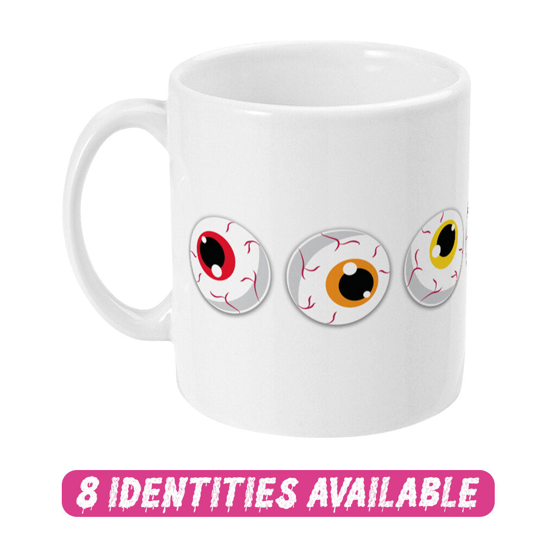 A white ceramic mug featuring three cartoon eyeballs with different coloured irises: one red, one orange, and one yellow. The design showcases playful and spooky elements. Below the mug, the text "8 IDENTITIES AVAILABLE" is displayed in bold, dripping pink letters, indicating that this design is part of a diverse collection with various options.