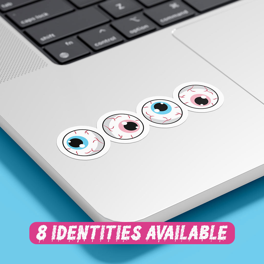 A close-up image of a laptop with four eyeball stickers placed on the bottom right corner of the device. The stickers feature cartoonish eyeballs with irises in colours representing the transgender flag: blue, pink, and white. At the bottom of the image, there is a text overlay that reads "8 IDENTITIES AVAILABLE" in bold pink letters against a light blue background.