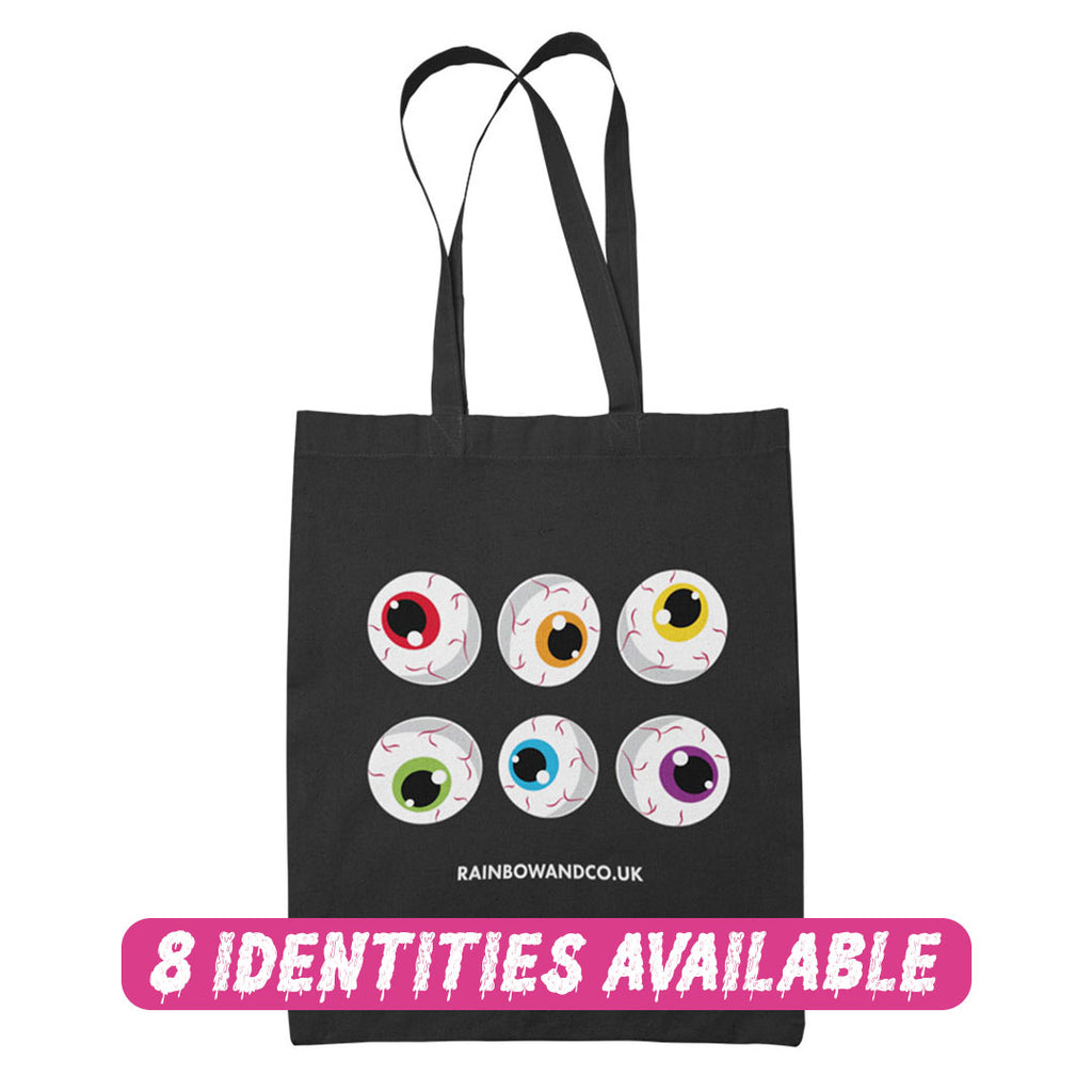 A black tote bag showcasing a collection of six cartoonish eyeballs arranged in two rows. Each eyeball has a unique colour: red, orange, yellow, green, blue, and purple. The text "RAINBOWANDCO.UK" is placed underneath the design, with a banner stating "8 IDENTITIES AVAILABLE".