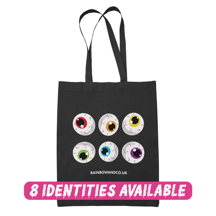 A black tote bag showcasing a collection of six cartoonish eyeballs arranged in two rows. Each eyeball has a unique colour: red, orange, yellow, green, blue, and purple. The text 