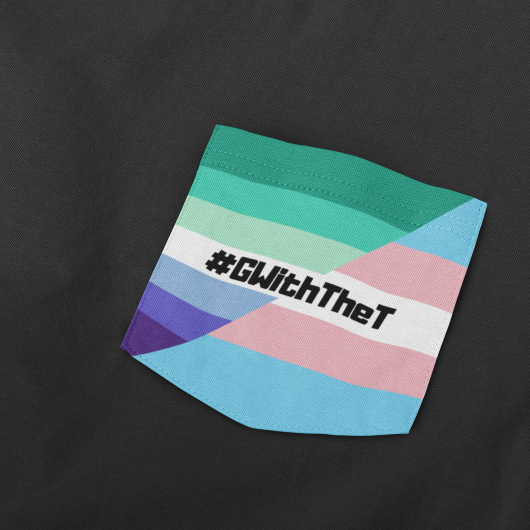Close-up of a black t-shirt featuring a stitched fabric pocket with the Gay Vincian Pride Flag and Transgender Pride Flag with the hashtag "#GWithTheT" printed in bold black text across the centre.