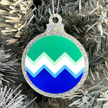 Load image into Gallery viewer, Close up of a white Christmas tree displaying a silver glitter bauble featuring a classic zig zag design in the colours of the gay pride flag.