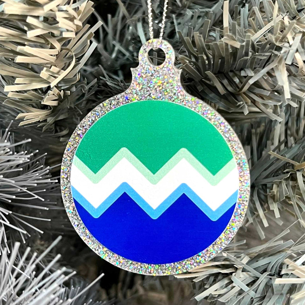 Close up of a white Christmas tree displaying a silver glitter bauble featuring a classic zig zag design in the colours of the gay pride flag.