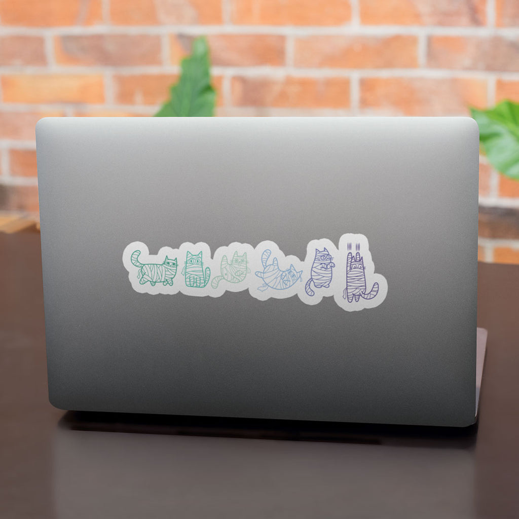 A laptop with several mummy cat stickers lined up on the bottom right corner. The cats are coloured in various shades of green and blue, symbolising the gay pride flag.