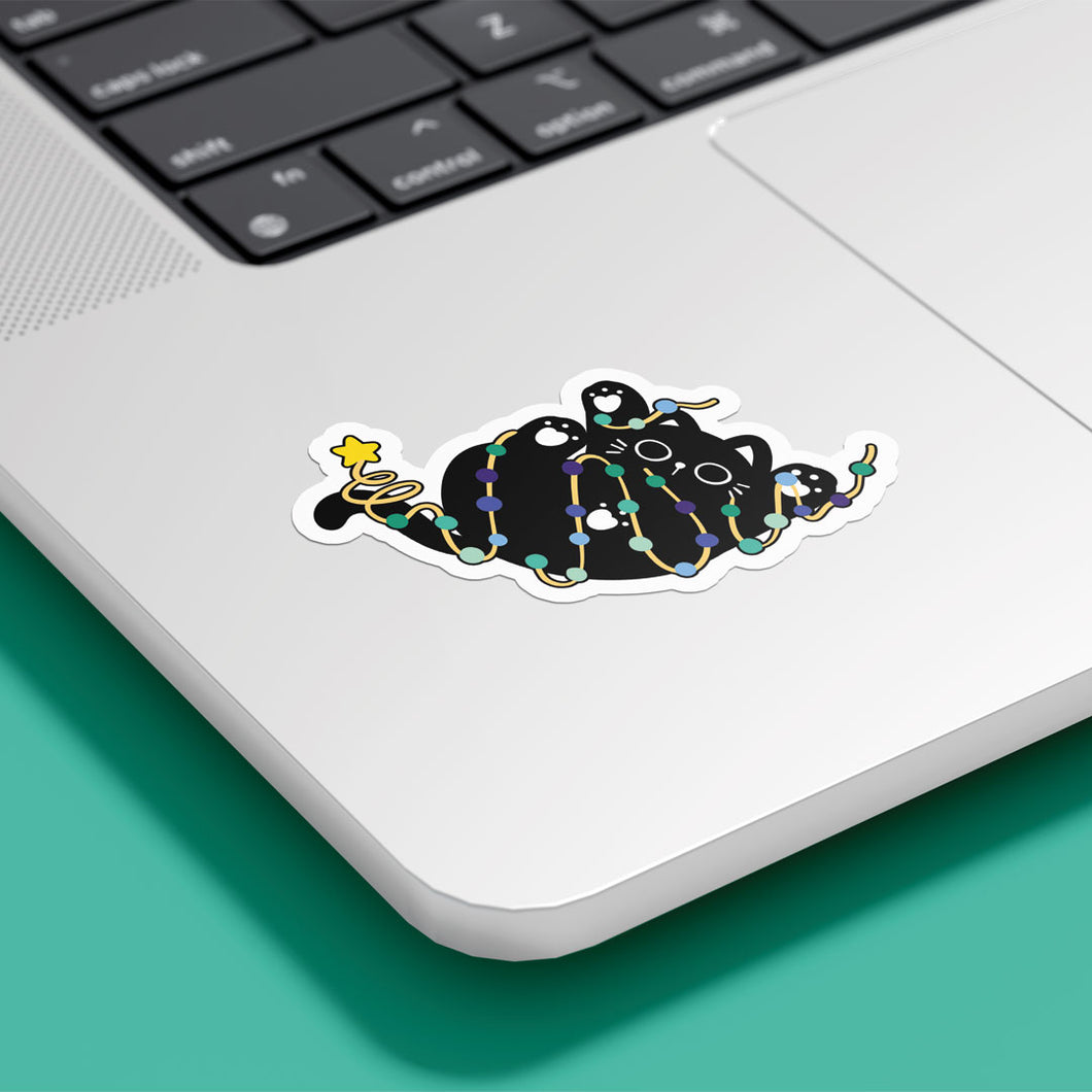 A cute black cat, wrapped in Gay pride-coloured string lights (shades of green, blue, and indigo), is lying on its back, reaching playfully. The sticker is shown on a silver laptop.