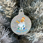 Close up of a white Christmas tree displaying a silver glitter bauble featuring retro text reading 'cosy vibes'. The image shows a mug of hot chocolate with marshmallows and a gingerbread man wearing a Santa hat. A candy cane in the mug and lights around the mug are the colours of the gay pride flag.