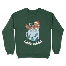 Load image into Gallery viewer, Bottle Green sweatshirt featuring retro text reading &#39;cosy vibes&#39;. The image shows a mug of hot chocolate with marshmallows and a gingerbread man wearing a Santa hat. A candy cane in the mug and lights around the mug are the colours of the gay pride flag.