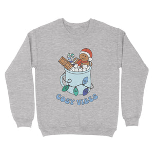 Heather Grey sweatshirt featuring retro text reading 'cosy vibes'. The image shows a mug of hot chocolate with marshmallows and a gingerbread man wearing a Santa hat. A candy cane in the mug and lights around the mug are the colours of the gay pride flag.