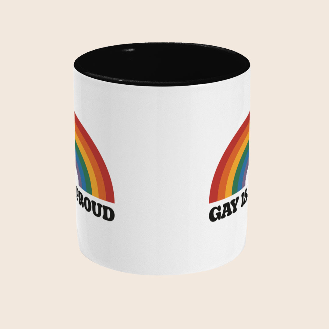 Front view of Gay Is Proud mug with black handle and interior, featuring a rainbow graphic above the words Gay Is Proud on a white ceramic mug