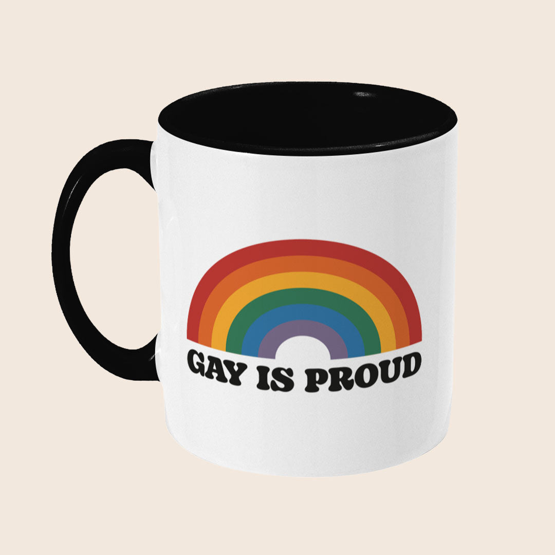 Angled side view of Gay Is Proud mug showing black handle, coloured interior, and wraparound rainbow design