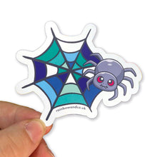 Load image into Gallery viewer, A hand holding a cute spider sticker with a gay pride web design. The web is decorated with shades of green, blue, and white, representing the gay pride flag.