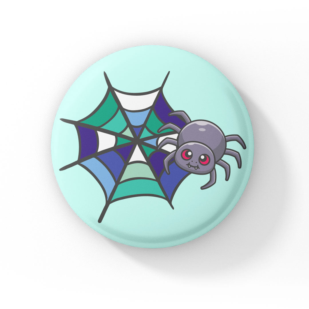 A circular badge showcasing a grey spider with pink eyes on a web coloured in green, white, blue, and navy, representing the gay pride flag. The badge has a mint green background.