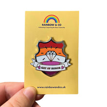 Load image into Gallery viewer, White hand holding up an enamel pin on a yellow backing card. The pin is in the shape of a shield with a banner across it&#39;s front. Banner reads Gay of Honor. The background of the pin is the lesbian pride flag and there is a jewel icon in the centre. The jewel and banner are filled with white glitter.